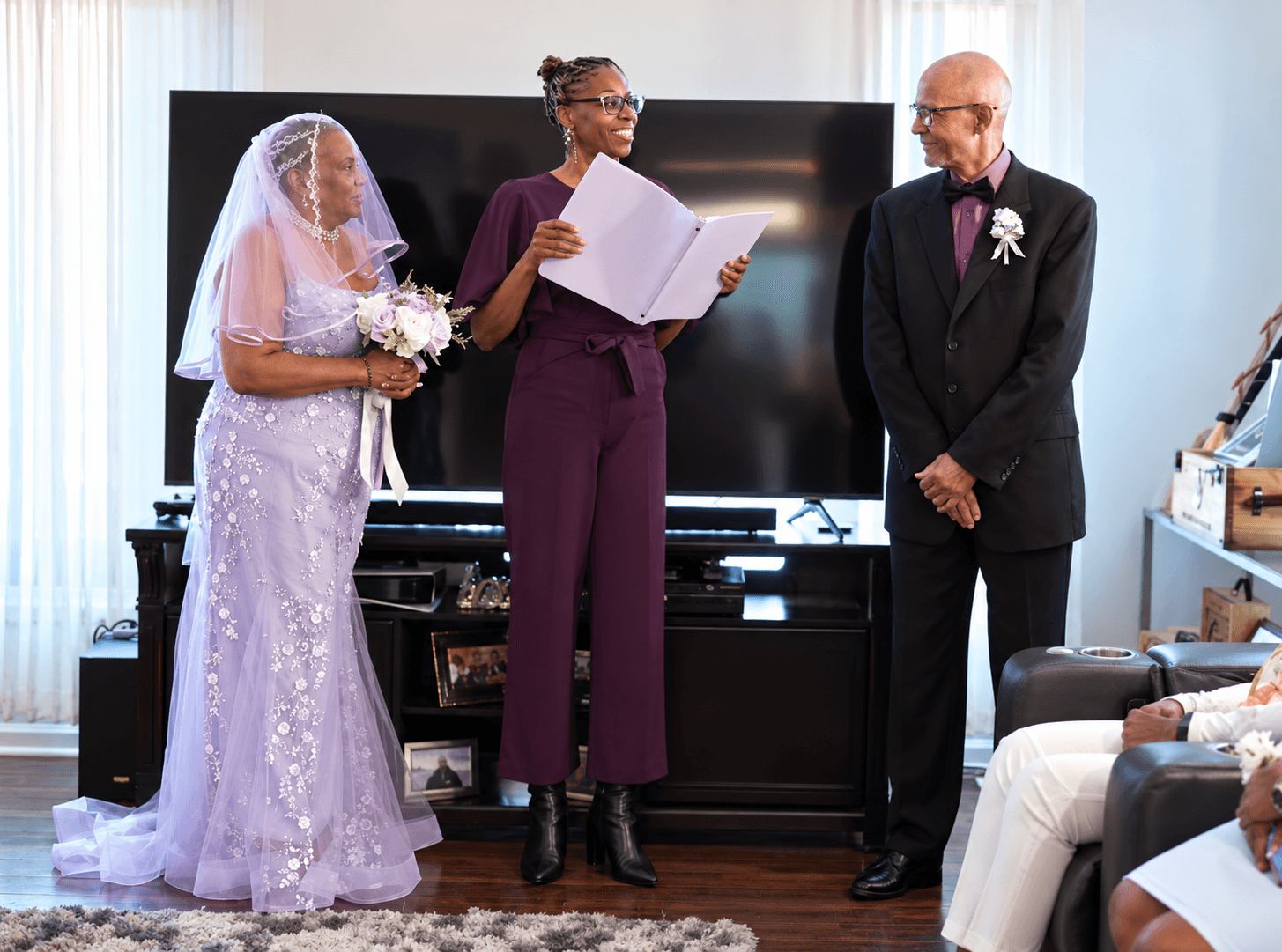 Older bride and groom stand with an officiant during an intimate home wedding ceremony.